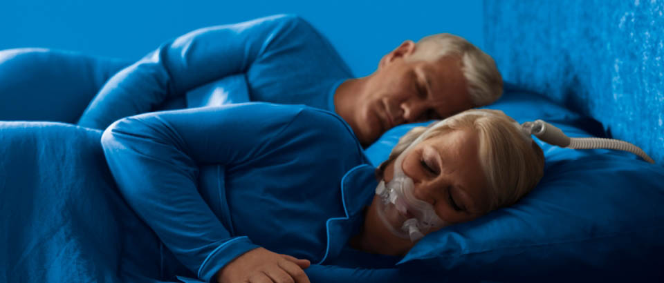 Women wearing blue sleeping on her side wearing a mask and a man wearing blue sleeping on his side
